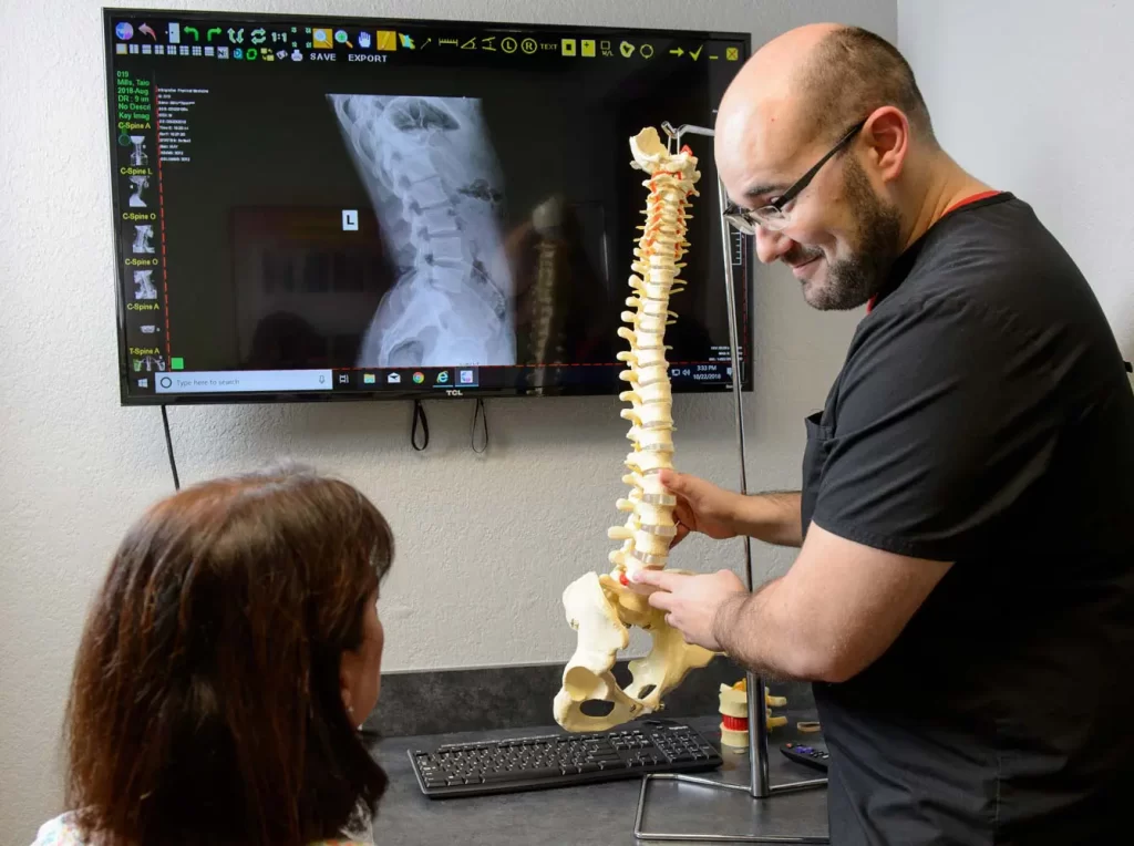 a man holding a model of a spine in front of a patient and xray scan