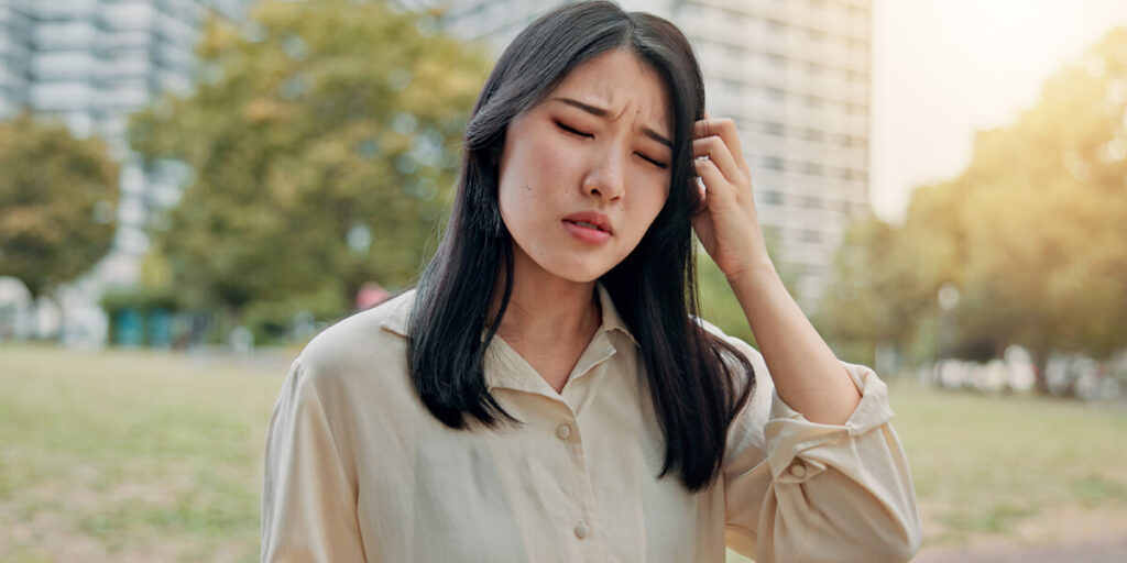 a woman outside holding the side of her head in pain